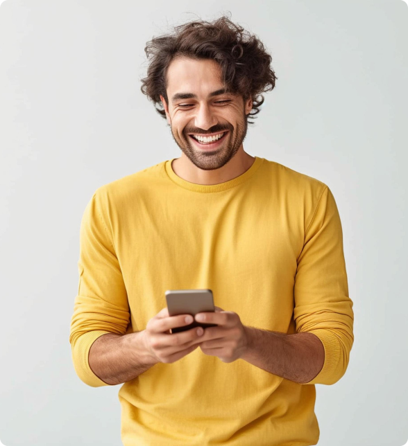 Smiling man in a yellow sweater looking at his phone, standing against a light background.